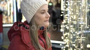 美丽迷人的女人站在一个装饰着花环的橱窗附近。 新年圣诞节。